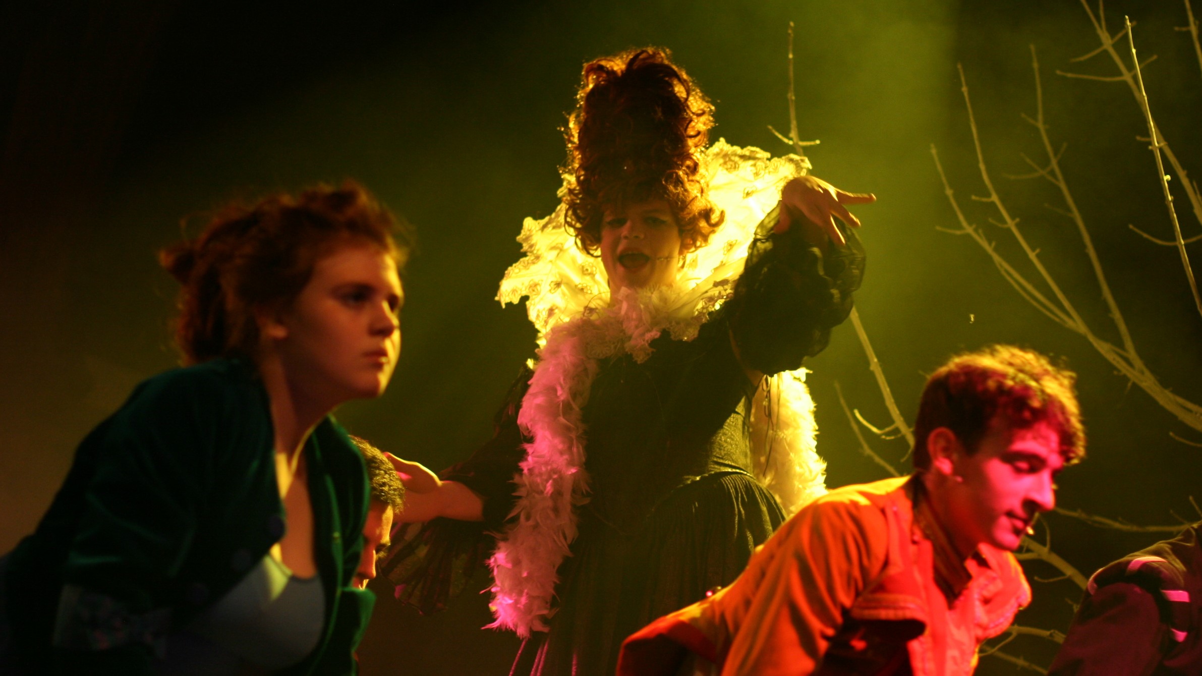 Romeo and Juliet: Lady Capulet stands tall in a beehive wig, backlit with green light, while in the foreground are blurred dancers mid-move