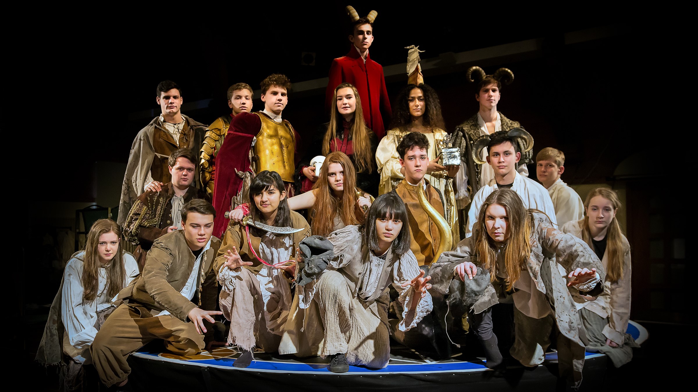 Doctor Faustus: a large group of intimidating and mostly drably-dressed "demons" crowded onto the stage and crawling off the front; Helen of Troy and the female Dr Faustus stand centre stage with the horned Mephistopheles towering above them in a red velvet coat