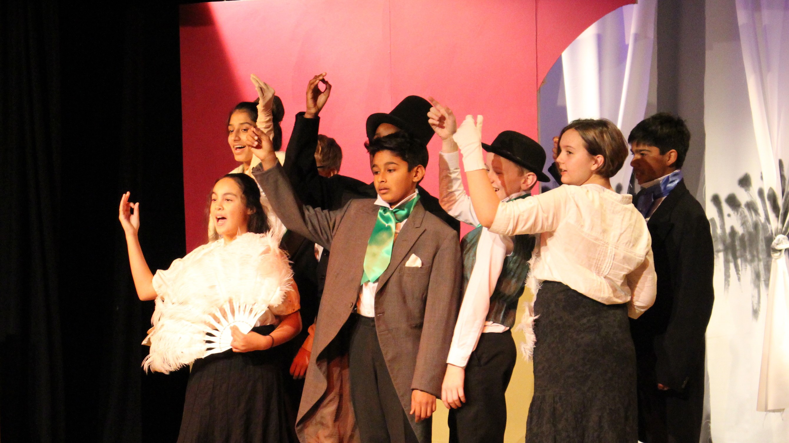 Great Expectations: Pip and other characters in a group centre-stage with hands raised to wave