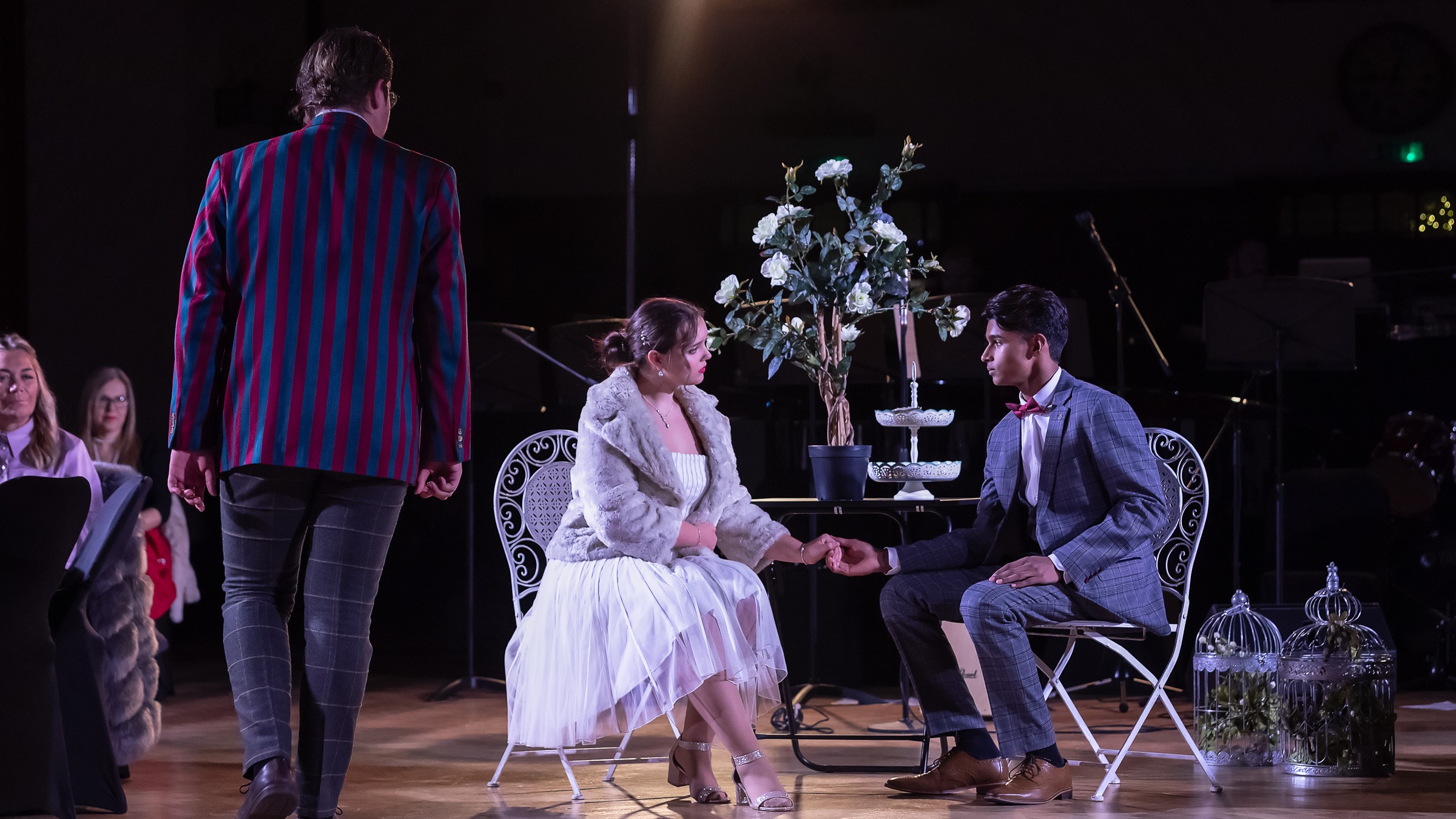 The Great Gatsby: Gatsby and Daisy talk while seated at a table, while Nick Carraway prowls by, watching them