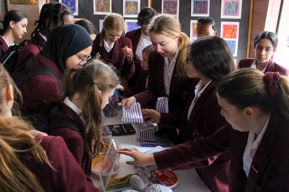 Year 7 pupils wearing maroon school uniforms working at a very busy stall selling sweets to their peers in school