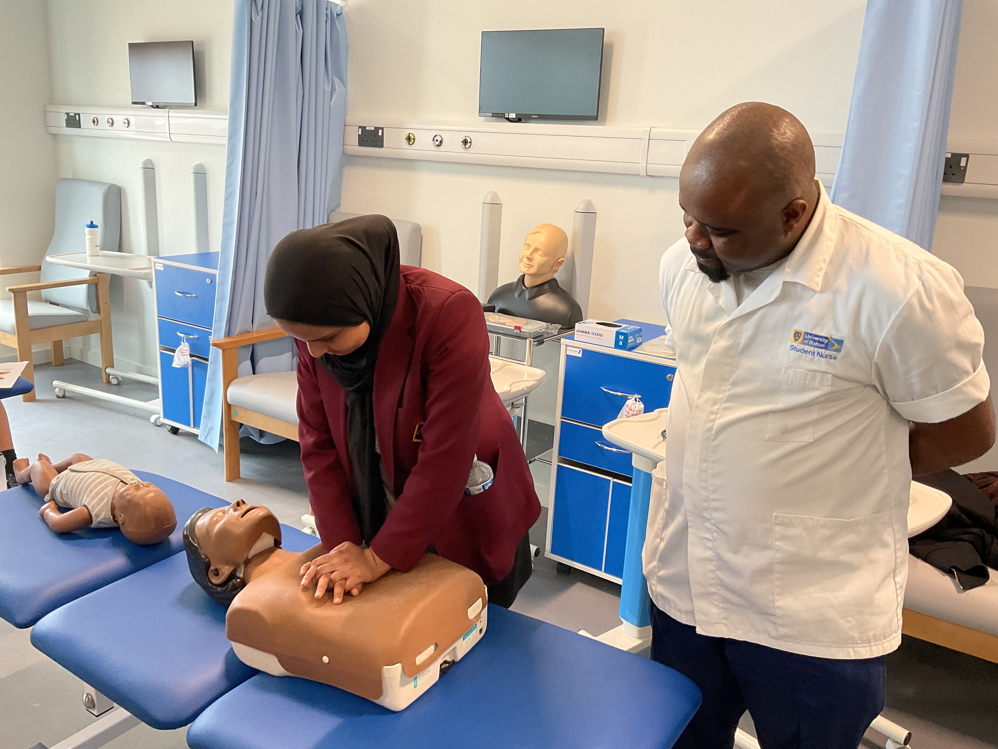 A girl in uniform performing CPR on a dummy while an adult watches 